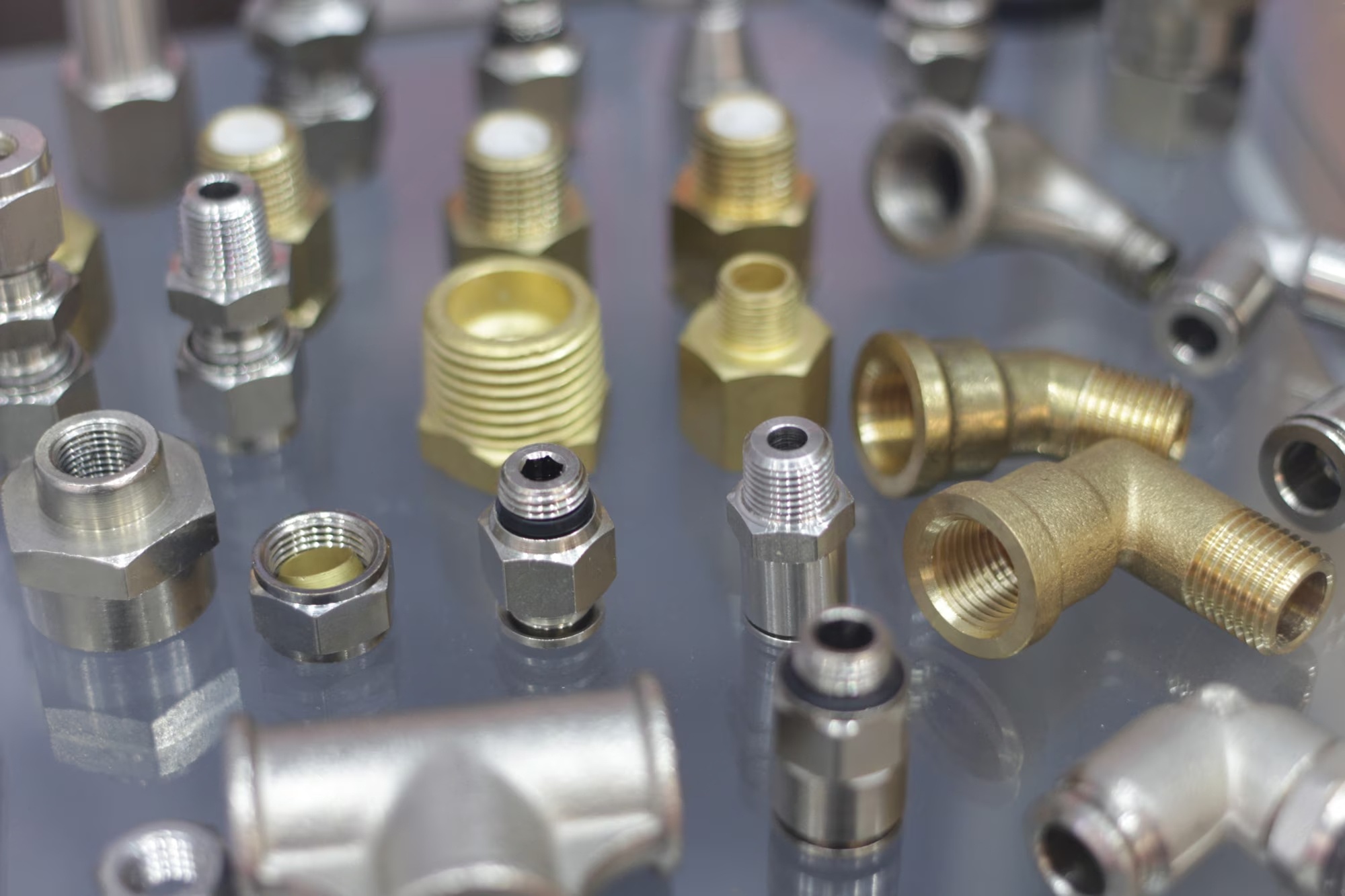 Collection of various stainless steel industrial fittings including elbows, tees, and flanges on a white reflective surface.