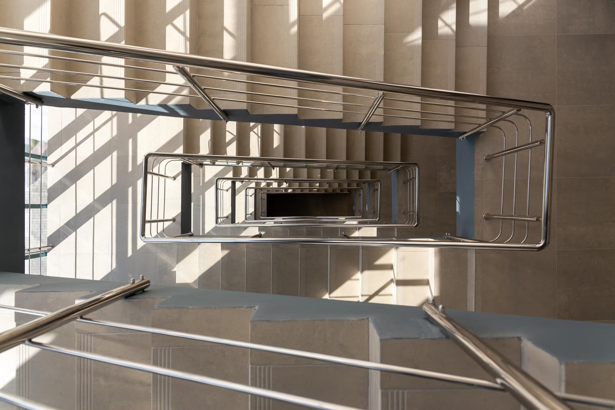 Modern architectural staircase with sleek stainless steel railings in a high-end commercial lobby with marble floors.